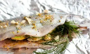 Pstrąg tęczowy filet z piekarnika, przygotowany z czosnkiem i koperkiem na folii aluminiowej.