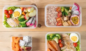 Cztery pojemniki z kolorowymi, zdrowymi posiłkami typu bentos: kurczak, ryż, warzywa i owoce.