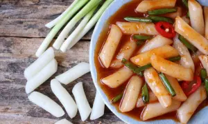 Pyszne kluski ryżowe tteokbokki w pikantnym sosie, podane z dymką i papryczką chili.