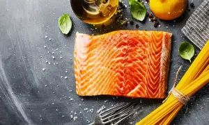 Świeży łosoś w plastrach, makaron spaghetti, cytryna, oliwa i bazylia na ciemnym tle. Idealne składniki na pyszny obiad.