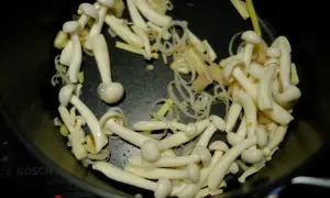 Grzybki shimeji smażą się na patelni z cebulką i imbirem, tworząc aromatyczne danie.