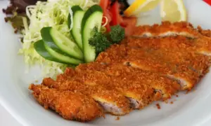 Chrupiący schab po japońsku, pokrojony w plastry, podany z sałatką z kapusty, ogórkiem, pomidorem i cytryną.