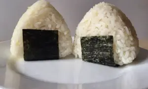 Dwa japońskie kulki ryżowe, onigiri, z kawałkami nori na białym talerzu.