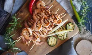 Grillowane krewetki po angielsku na szpadkach, podane z grillowaną cukinią, szparagami i papryczkami chili na drewnianej desce.