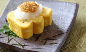 Tamago co to? Japoński omlet tamagoyaki, zwinięty w rolki, podany z tartą rzodkwią i grzybami enoki na talerzu z bambusowym wzorem.