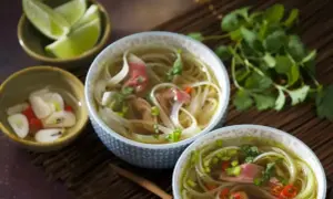 Dwie miseczki aromatycznej zupy pho, z cienkim makaronem ryżowym, plastrami wołowiny i świeżą kolendrą. Obok miseczki z limonką i marynowanym imbirem. To przepis na oryginalną zupę pho.