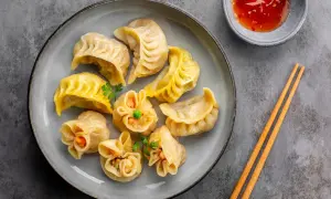 Talerz pełen różnorodnych pierożków dim sum, ozdobionych natką pietruszki, z miseczką sosu i pałeczkami.