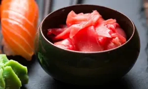Miseczka z różowym, marynowanym imbirem obok sushi z łososiem i zielonym wasabi.