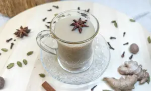 Aromatyczny napój, czyli chai, w szklanej filiżance z anyżem. Wokół przyprawy: kardamon, goździki, cynamon, imbir.