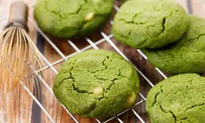 Zielone, japońskie ciasteczka matcha z kawałkami białej czekolady na metalowej kratce, obok bambusowej miotełki do herbaty.
