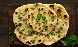 Stos chlebków naan, posypanych kolendrą i czarnuszką, z widocznymi pęcherzykami powietrza. Idealne do curry, ale warto sprawdzić chlebek naan kcal.