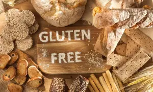 Różnorodne pieczywo i przekąski, na desce napis "GLUTEN FREE". Dowiedz się, co to jest gluten i jak go unikać.