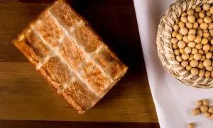 Wędzone tofu z kratką na drewnianym tle, obok koszyczek z ziarnami soi. Idealne do zdrowych posiłków, niskokaloryczne.