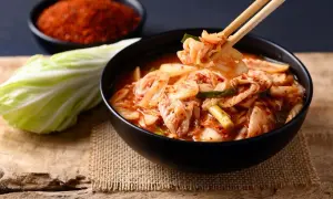 Miseczka z kimchi, pałeczki podnoszące kawałek kapusty, liść kapusty i miseczka z przyprawą.