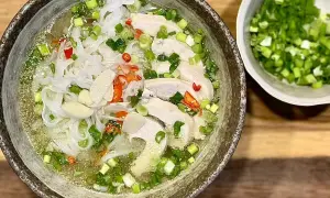 Aromatyczna zupa pho ga z kawałkami kurczaka, makaronem ryżowym, szczypiorkiem i papryczką chili. Obok miseczka z posiekanym szczypiorkiem.