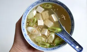 Miseczka z bulionem miso, kostkami tofu, zieloną cebulką i sezamem, trzymana w dłoni.