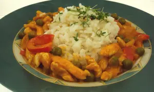 Pyszne tajskie curry z kurczakiem, podane z ryżem i zielonym groszkiem. Danie ozdobione jest świeżymi ziołami.