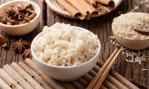 Miseczka parującego congee, obok miseczki z ryżem, anyżem i laskami cynamonu.