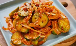 Pikantne ogórki po koreańsku, z cebulą i sezamem, na jasnoszarym talerzu.