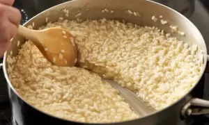 Gotuje się kremowy ryż do risotto w garnku, mieszany drewnianą łyżką.