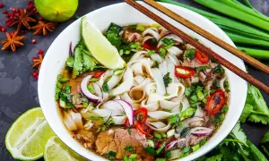 Aromaticzny makaron pho z wołowiną, świeżą kolendrą, cebulą i chili. Podany z limonką i pałeczkami.