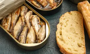 Otwarta puszka ryb wędzonych, obok kromki chleba. Czy ryby wędzone a cholesterol to temat do dyskusji?