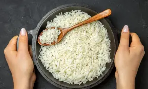 Dwie dłonie trzymają okrągłą patelnię z parującym ryżem basmati. Drewniana łyżka zanurzona w ryżu.