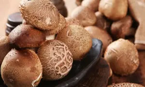Kupa świeżych grzybów shiitake na czarnej desce, niektóre w worku jutowym.