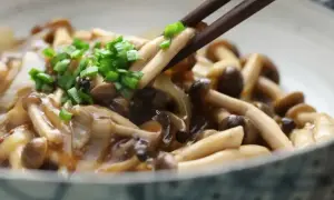 Chopsticks podnoszą pyszne, duszony chińskie grzyby, posypane zieloną cebulką.