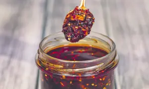 Łyżeczka z aromatycznym chili w oleju nad słoikiem pełnym tej pikantnej przyprawy.