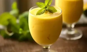 Gęsty, kremowy mango lassi w kieliszku, ozdobiony listkami mięty. Idealny na orzeźwienie.