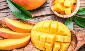 Soczyste, pokrojone w kostkę i plastry mango, które pokazuje, co to jest mango. Całe, dojrzałe owoce i liście na drewnianym tle.