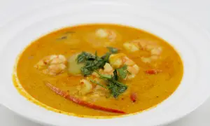 Aromatyczna zupa tom yum z krewetkami, ozdobiona świeżą kolendrą i kawałkami chili, podana w białej misce.