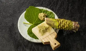 Świeżo starty chrzan japoński na tradycyjnej tarce. Obok liść i kawałek korzenia wasabi.