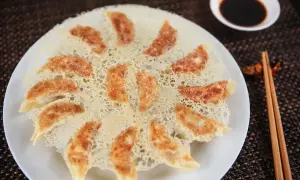 Chrupiące pierożki gyoza ułożone na talerzu, z chrupiącą panierką z ciasta. Obok miseczka sosu sojowego i pałeczki.