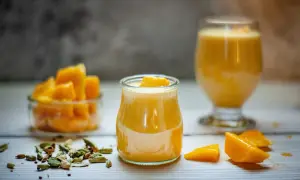 Słodki jogurt z mango, udekorowany kawałkami owoców, obok miseczki z mango i kardamonu.