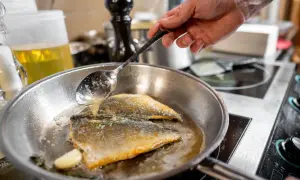 Szef kuchni polewa łyżką ryby na patelni, przygotowując najsmaczniejsze ryby do smażenia.