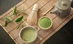 Tradycyjny zestaw do parzenia matchy: bambusowa miotełka, czarka z napojem, drewniana łyżeczka, czajniczek i miseczka z zielonym proszkiem, z którego jest matcha.