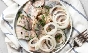 Pyszny śledź a'la matjas na talerzu, udekorowany krążkami cebuli i koperkiem. Gotowy do podania z widelcem obok.