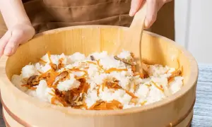 Mieszanie ryżu z marchewką i grzybami w drewnianej misce, przygotowanie zaprawy do sushi.