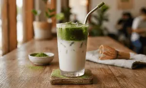 Przepis na iced matcha latte: zielony napój z mlekiem i lodem, obok miseczka z matchą i bambusowa miotełka.