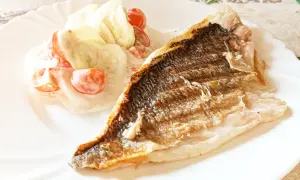 Dorada grillowana z chrupiącą skórką, podana z orzeźwiającą sałatką z pomidorków i ogórka w sosie.