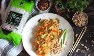 Pyszny pad thai z wołowiną, makaronem ryżowym i orzeszkami ziemnymi. Obok składniki: makaron, sos i płatki chili.