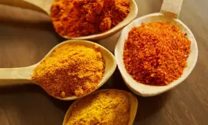 Drewniane łyżki wypełnione przyprawami: intensywnie żółta kurkuma i pomarańczowe proszki, idealne do aromatycznego curry.