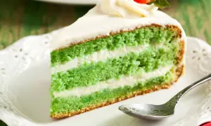 Zielone ciasto z matcha i mascarpone, przełożone kremem, ozdobione bitą śmietaną i truskawką.