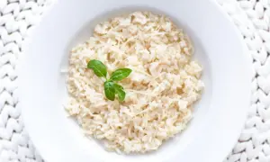 Ryż parboiled co to? Gotowany ryż z parmezanem i listkiem bazylii na białym talerzu.