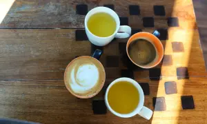 Kawa i herbata na drewnianym stole. Czy zielona herbata pobudza? Obok kawy latte i czarnej, dwie filiżanki z zieloną herbatą.