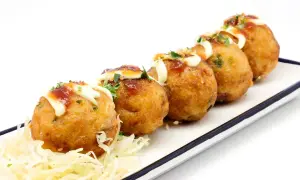 Pięć złotych kulek takoyaki, polanych majonezem i sosem, na białym talerzu z poszatkowaną kapustą. Idealne japońskie przekąski, przepisy na nie są proste!