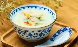 Misternie zdobiona miseczka z congee, czyli tradycyjną azjatycką owsianką z warzywami. Obok leży łyżka.