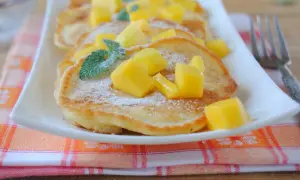 Puszyste placuszki z cukrem pudrem i kostkami mango, ozdobione listkami mięty. Idealne śniadanie z mango.